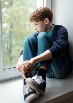 Boy sitting on window sill thinking why is teen mental illness soaring
