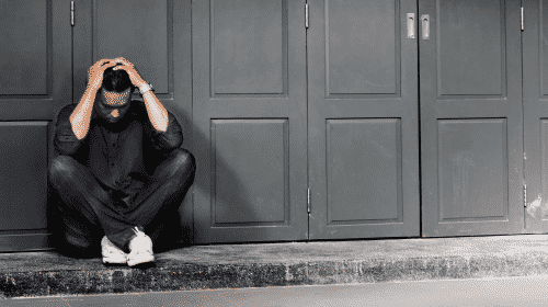 troubled man outside sitting down holding his head