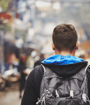 young man with backpack walking in city