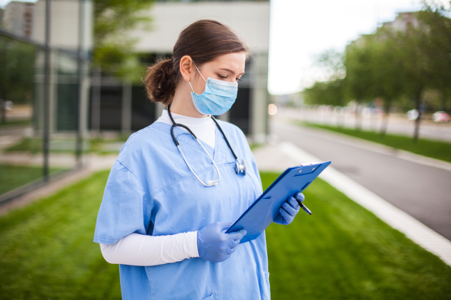 A doctor in blue scrubs writes something on a clipboard
