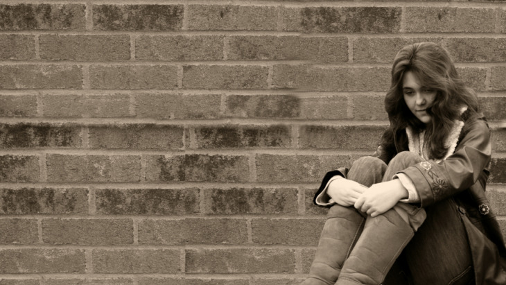 A depressed looking woman sits against a brick wall