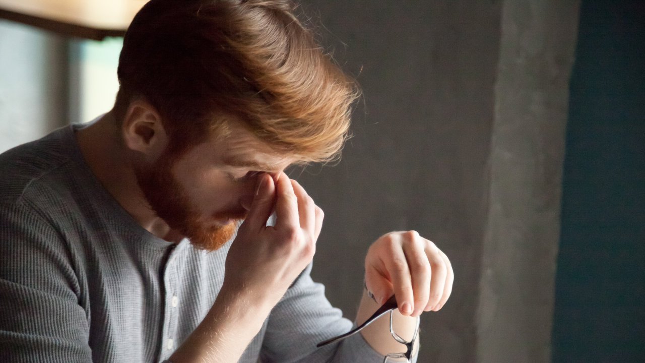 A man clutches the bridge of his nose, dizzy with headaches