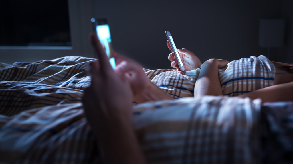 Two people lying in bed, staring at their phones