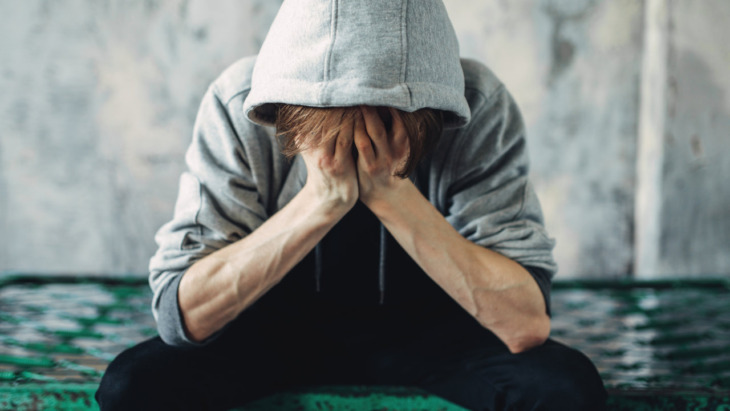 A depressed person sitting on a bed clutches their face in their hands
