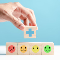 Person placing a block with a medical cross on it atop a row of blocks showing faces with different moods