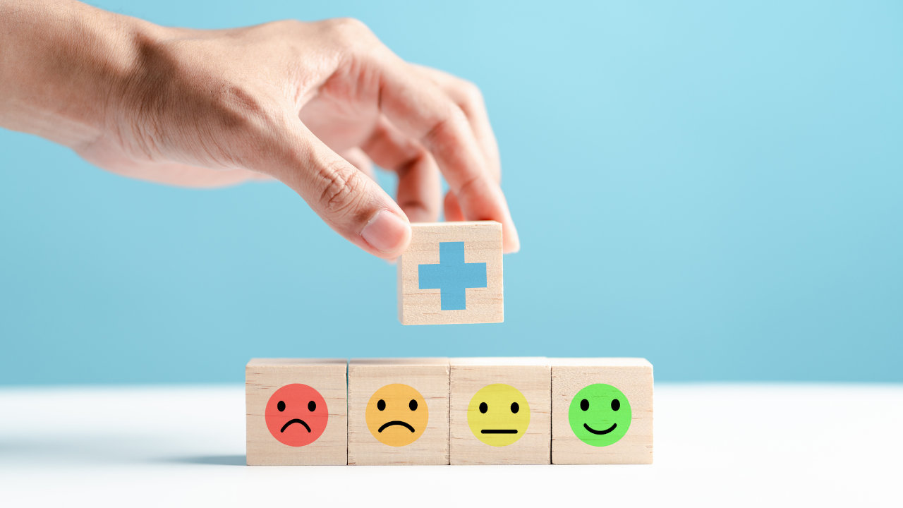 Person placing a block with a medical cross on it atop a row of blocks showing faces with different moods
