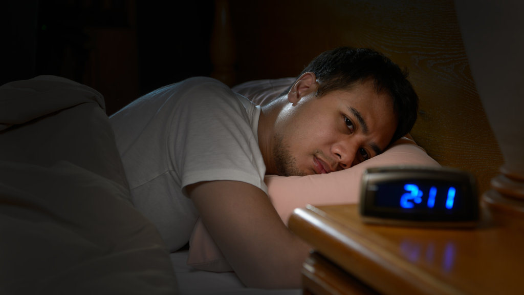A man struggling with insomnia, lying awake in bed. Sleeping pill rehab can help with recurrent insomnia symptoms.