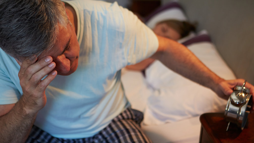 A man clutches his head as he struggles to sleep in bed.