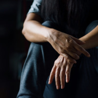 A depressed man against a dark background. Learn more about the link between trauma and addiction here.