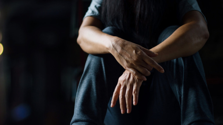 A depressed man against a dark background. Learn more about the link between trauma and addiction here.