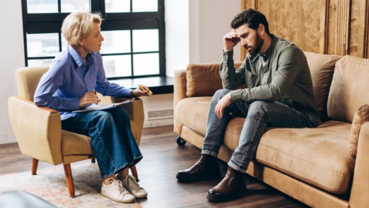 A mean clutches his head while speaking with a counselor