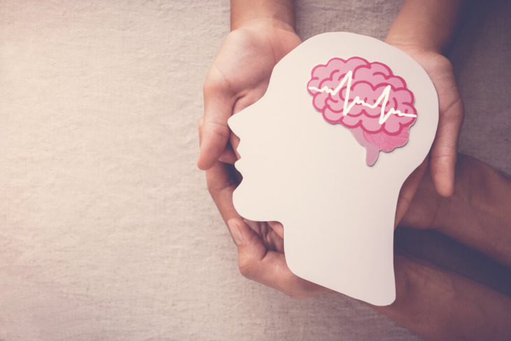 A person holding a graphic of a head with a brain. Learn more about ADHD and addiction here.