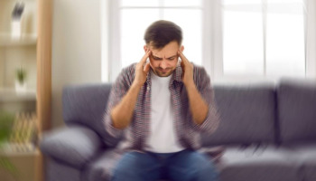 A man sitting on a couch grips his head. Learn more about gabapentin withdrawal here.