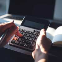 A person typing on a calculator at a home office. Learn more about how much rehab with cost without insurance in 2026 here