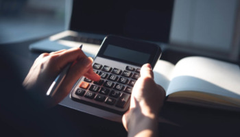 A person typing on a calculator at a home office. Learn more about how much rehab with cost without insurance in 2026 here