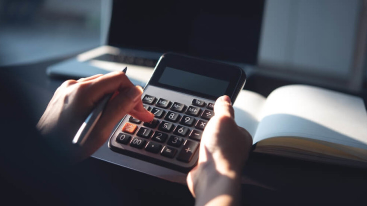 A person typing on a calculator at a home office. Learn more about how much rehab with cost without insurance in 2026 here