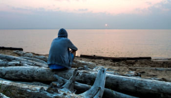 A man sits alone on a beach. Learn more about xylazine withdrawal symptoms here