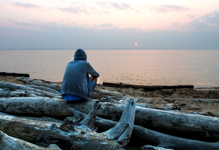 A man sits alone on a beach. Learn more about xylazine withdrawal symptoms here