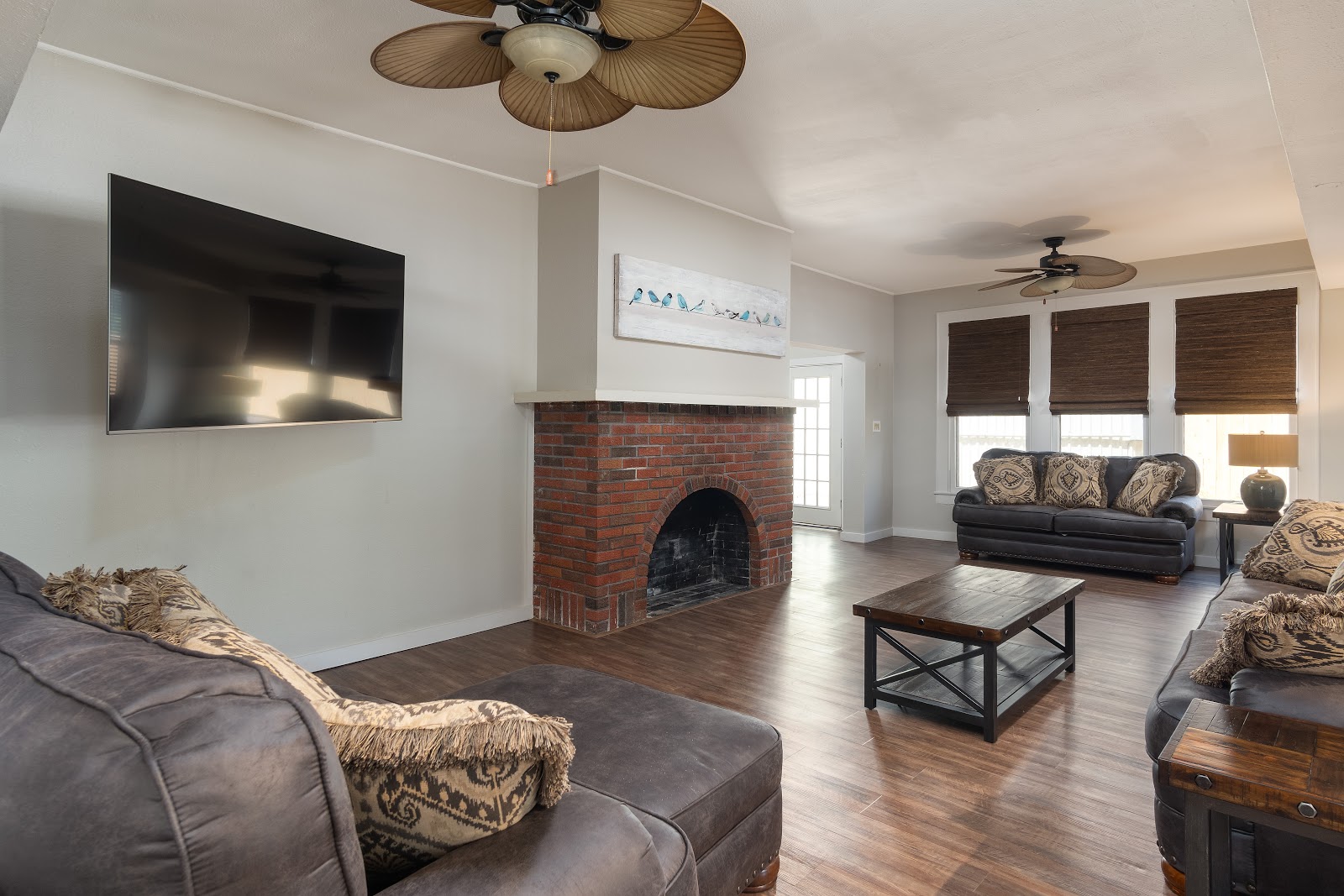 Interior common lounge with dark leather sofas, fireplace with brick surround, wood flooring, and television