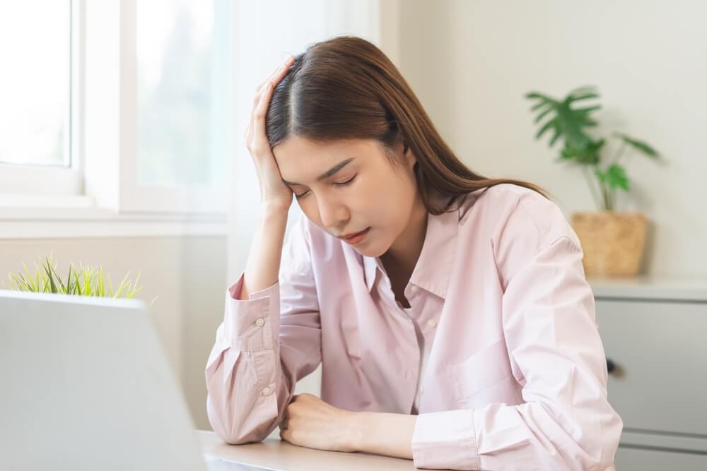 A woman grips her head, suffering from a headache. Learn more about functional alcoholism, including signs and when to get help, here.