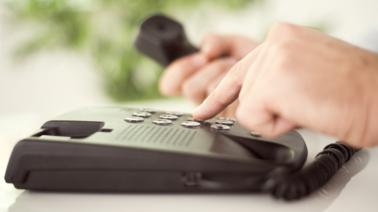 A person dials a number on a landline phone.