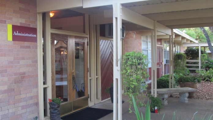 Exterior view of administration building entrance with brick facade, wooden doors, and covered porch area with landscaping
