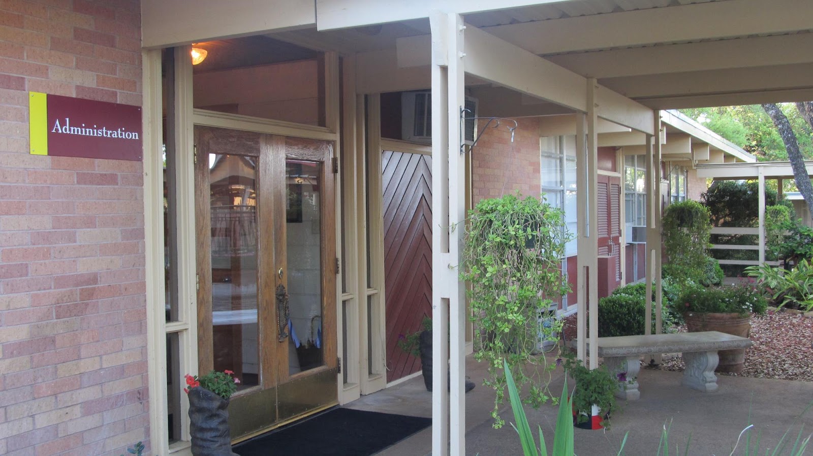 Exterior view of administration building entrance with brick facade, wooden doors, and covered porch area with landscaping