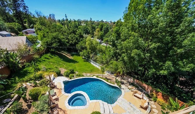 Overhead exterior view of swimming pool with spa, landscaped grounds, trees, and facility buildings
