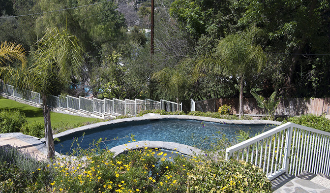 Exterior backyard landscape showing swimming pool with safety railings, manicured lawn, and surrounding vegetation