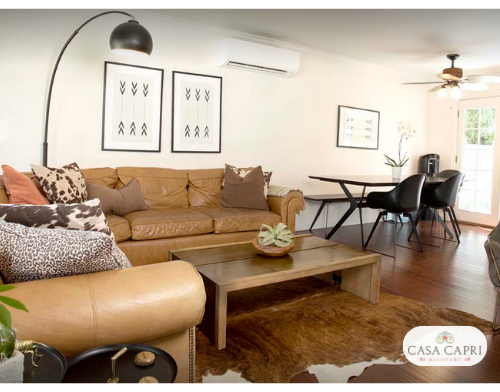 Interior social space featuring tan sectional sofa, large glass doors opening to outdoor patio, modern furnishings and Casa Capri logo