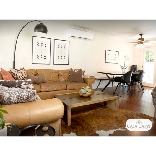 Interior social space featuring tan sectional sofa, large glass doors opening to outdoor patio, modern furnishings and Casa Capri logo