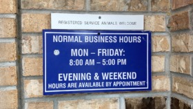 Exterior brick wall with business hours sign and service animals welcome notice mounted on building entrance