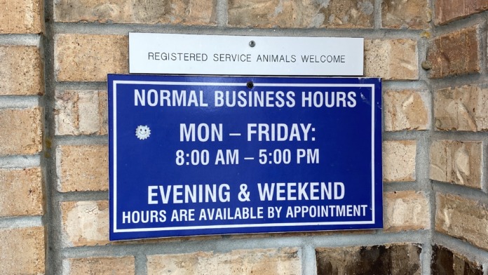 Exterior brick wall with business hours sign and service animals welcome notice mounted on building entrance