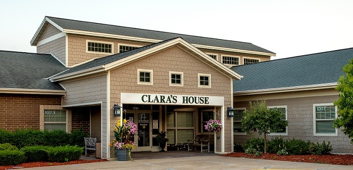 Exterior front entrance of Clara's House showing central portico, signage, flower baskets, and architectural details with surrounding landscaping