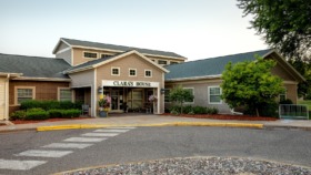 Exterior view of Clara's House treatment facility showing brick and siding construction, main entrance with covered portico, landscaped grounds, and parking area