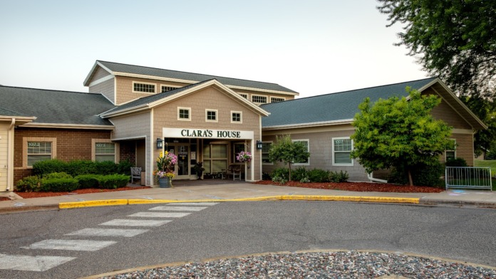 Exterior view of Clara's House treatment facility showing brick and siding construction, main entrance with covered portico, landscaped grounds, and parking area