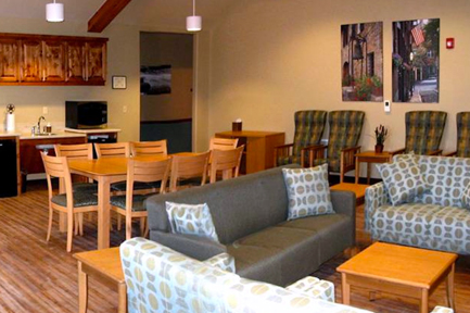 Interior common space with multiple dining tables, wooden chairs, activity board, and serving counter area
