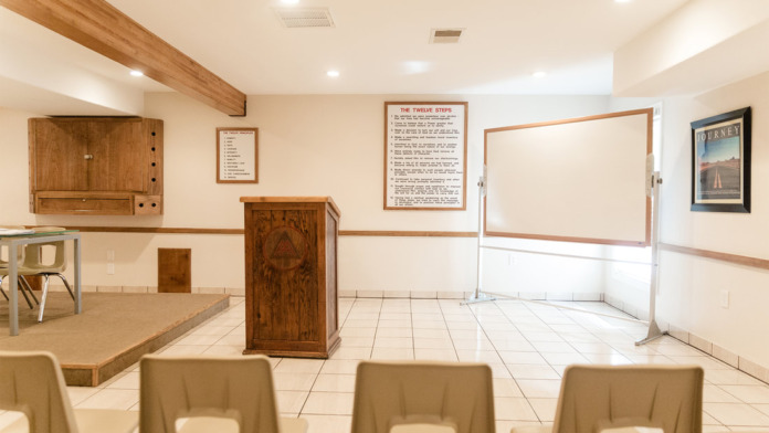 Interior group room with light wooden furnishings, recovery program materials on walls, tile flooring, and open space for group activities
