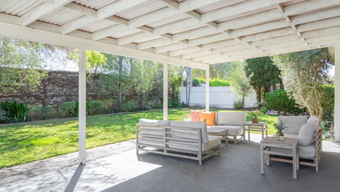 Exterior covered patio with white beam structure, comfortable seating furniture, views of manicured lawn and landscaping
