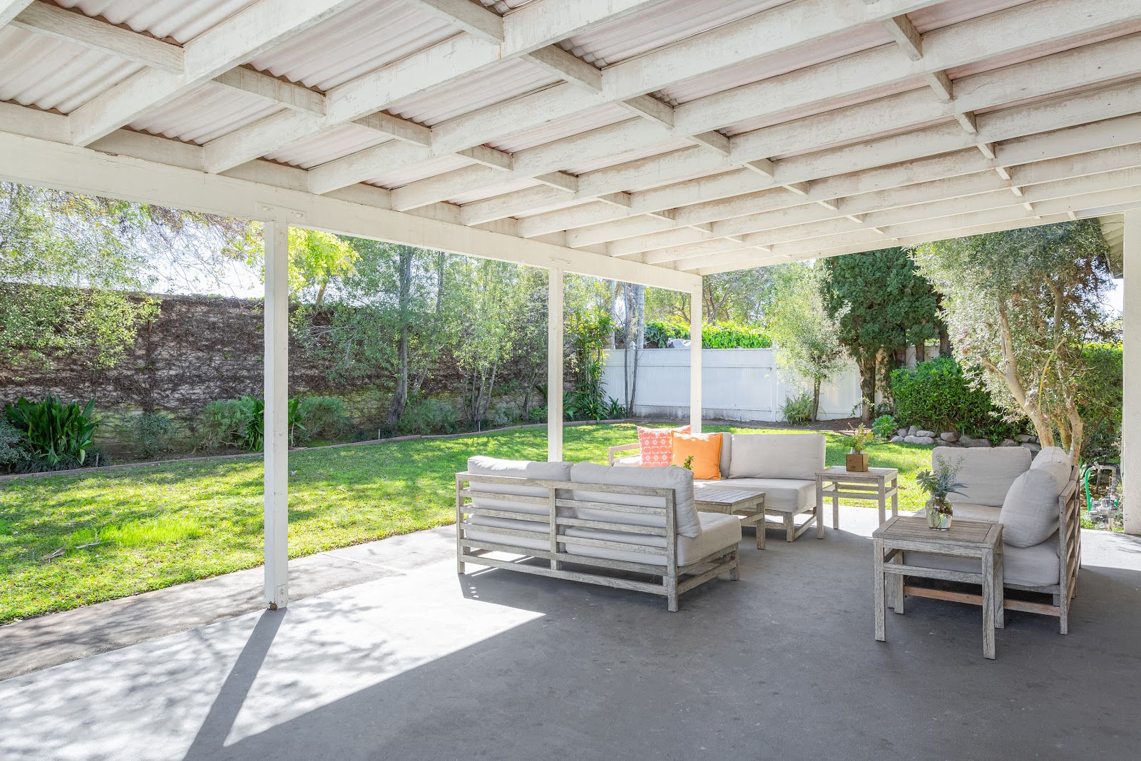 Exterior covered patio with white beam structure, comfortable seating furniture, views of manicured lawn and landscaping