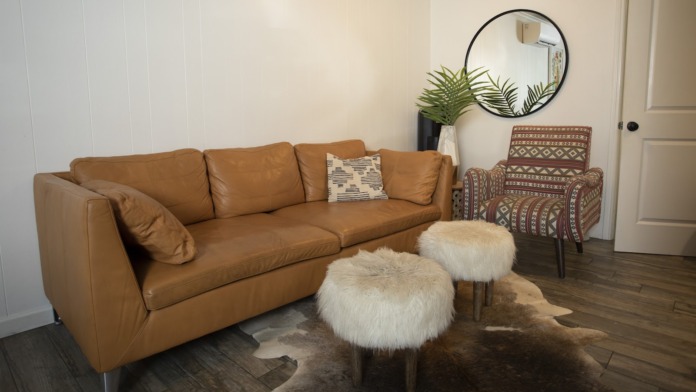 Interior lounge featuring oversized tan leather sectional sofa, wooden door, large windows with drapes, artwork, and accent chairs