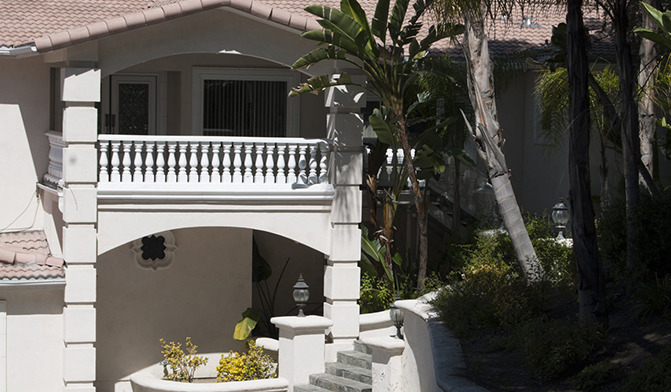 Exterior architectural detail showing white entrance archway with balcony, Mediterranean-style design elements, and landscaping