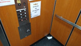 Interior elevator with wood paneling, control buttons, and facility signage including restroom access information for members only