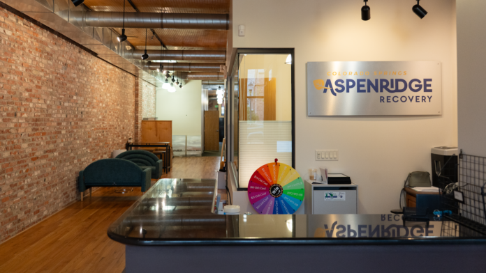 Interior reception desk with AspenRidge Recovery signage, hallway with brick walls, and modern office furnishings