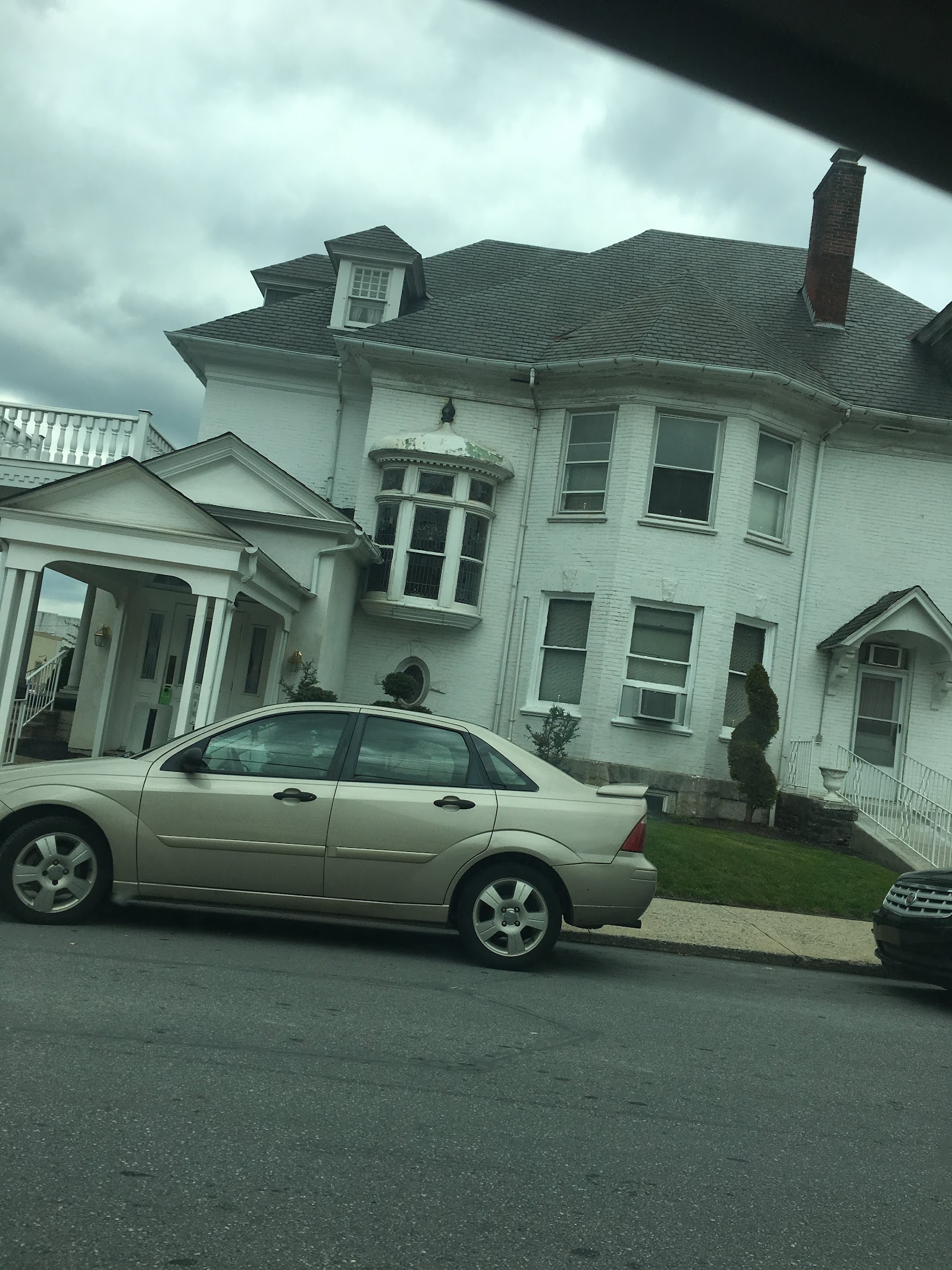 Exterior view of white Colonial-style building with multiple windows, dormer, covered entrance portico, and parking area