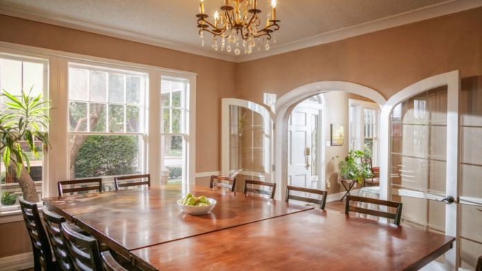 Interior formal dining space with large wooden table, chairs, arched doorways, chandelier, and large windows overlooking grounds