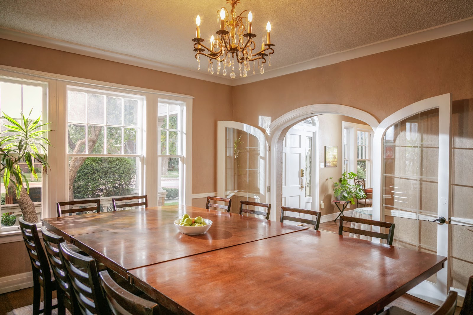 Interior formal dining space with large wooden table, chairs, arched doorways, chandelier, and large windows overlooking grounds