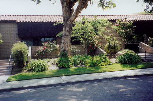 Exterior view of treatment facility showing front entrance with stone building facade, mature tree, manicured landscaping, and paved courtyard area