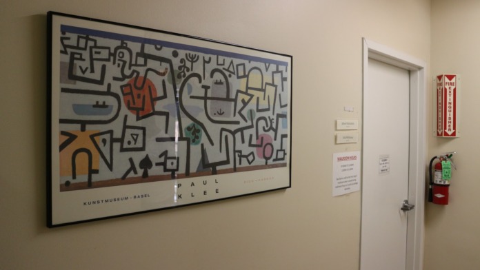 Interior corridor with metal fencing displaying student artwork including abstract designs, street scenes, and eye artwork with concrete columns
