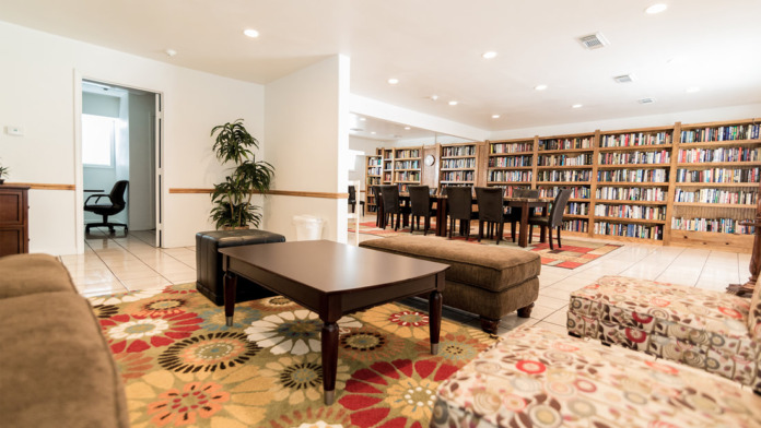 Interior common space with extensive bookshelves, library seating, dark upholstered chairs, colorful patterned rugs, and wooden finishes